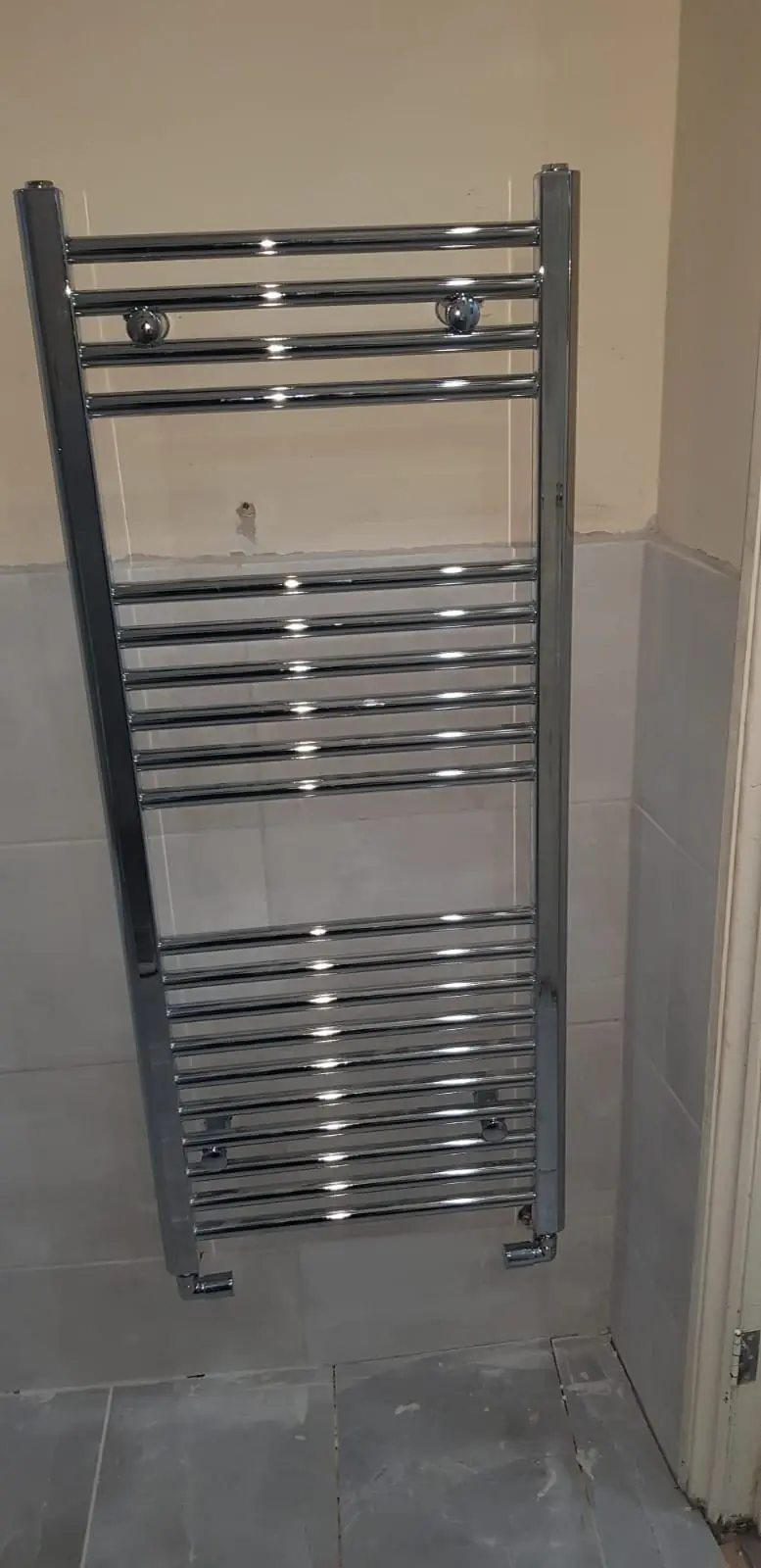Chrome heated towel radiator installed in a tiled bathroom