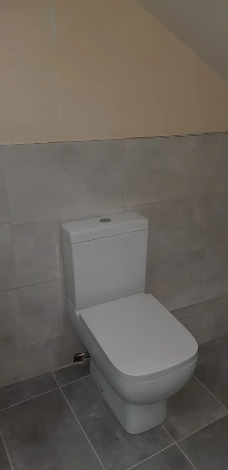 Close-coupled toilet installed in a grey tiled bathroom